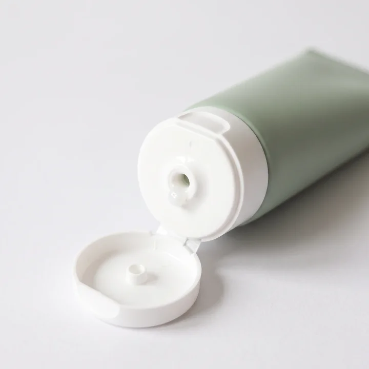 흰 배경 위에 눕힌 핸드크림 튜브의 열린 흰 뚜껑과 크림이 조금 묻은 입구를 가까이에서 찍은 제품 사진 촬영 예시