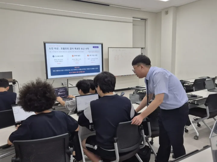 강사가 학생 옆에서 노트북 화면을 보며 '프롬프트 없이 목표만 보고 시작' 도전 미션을 지도하는 모습